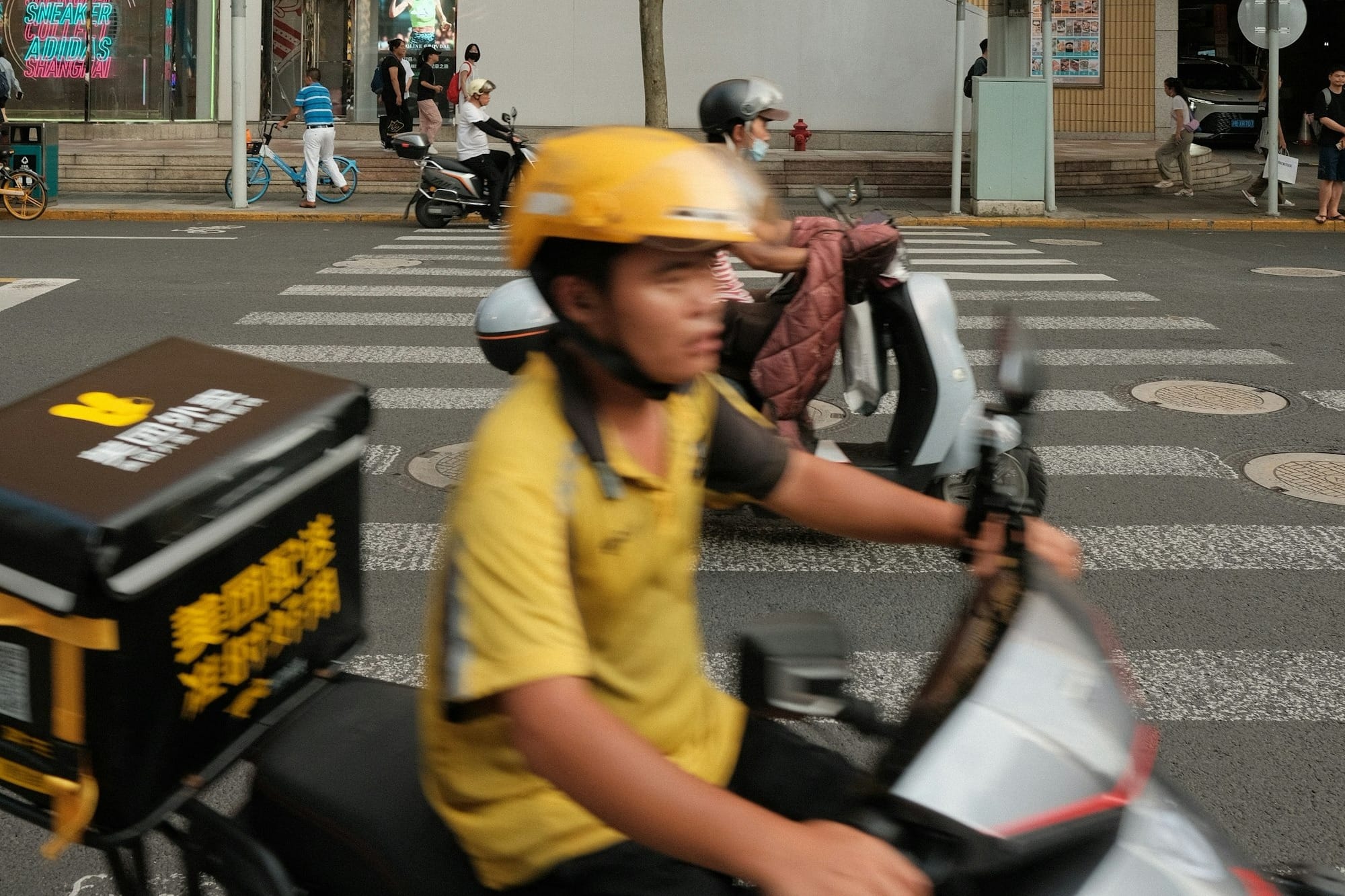 A man riding a scooter down a street next to a traffic light