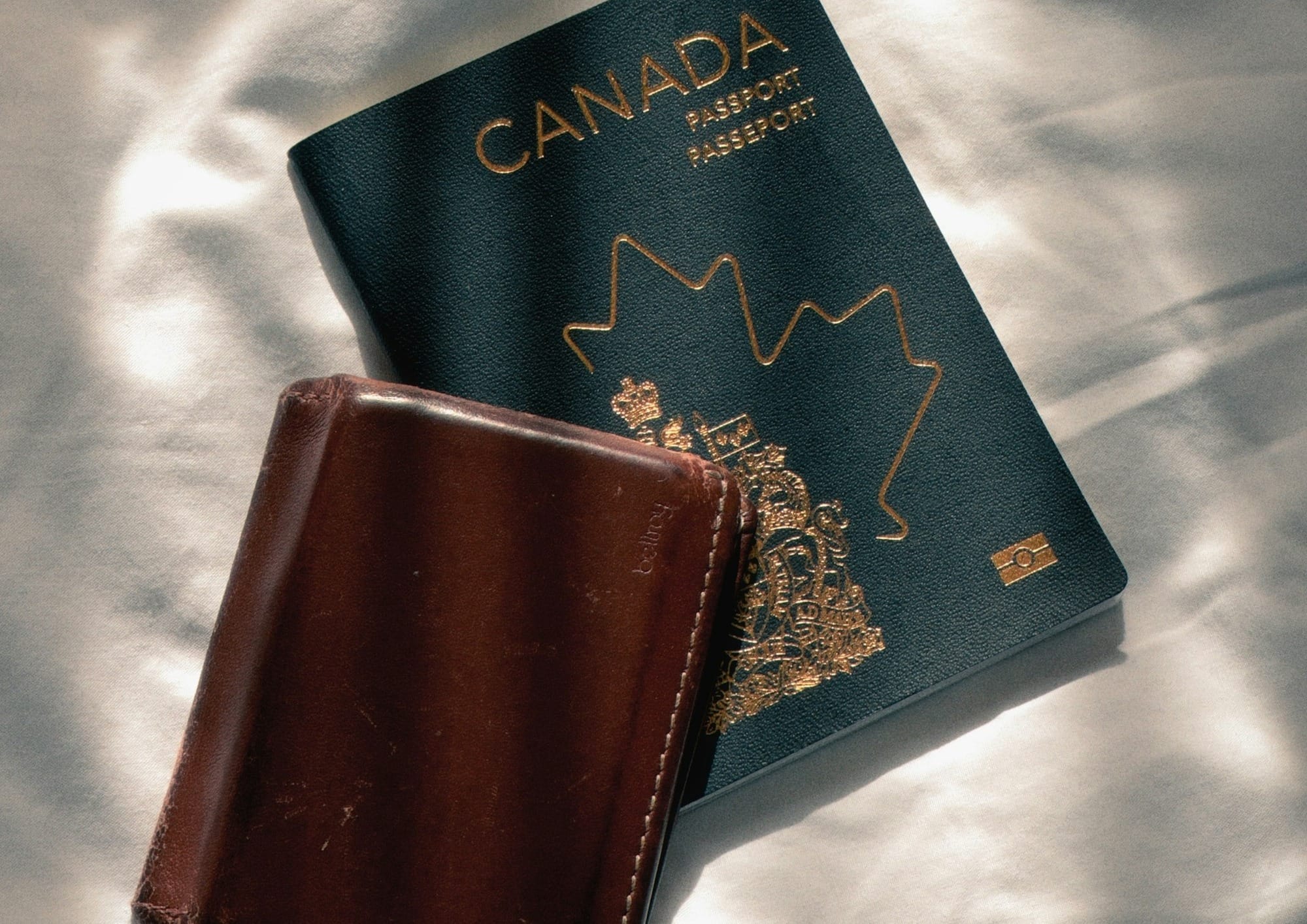 Canadian passport and brown leather wallet on white fabric.